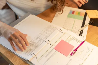 Close-up of an employee sorting documents with sticky notes and pens on a wooden desk.